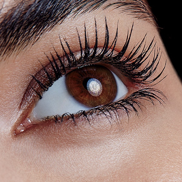 Close up of a woman's brown eye as she looks upwards, showing off very long and dark eyelashes