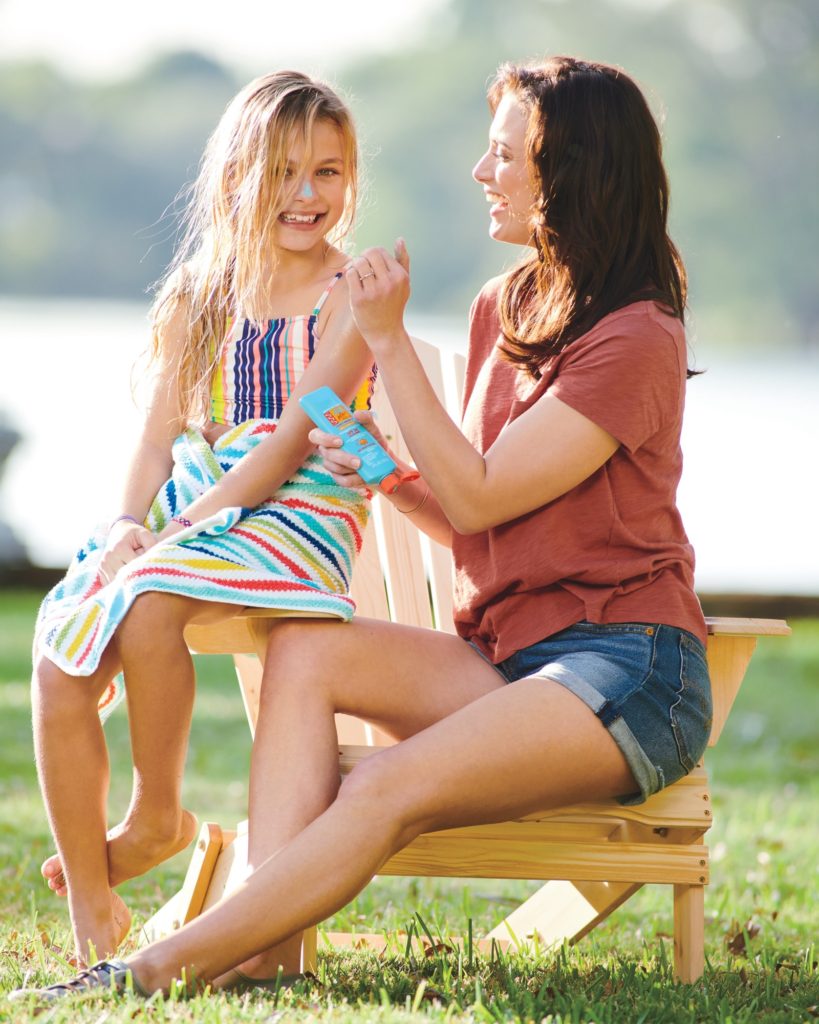 A mother sitting with her child as she helps her apply Bug Guard Plus IR3535® Cool 'N Fabulous™ Disappearing Color Lotion SPF 30