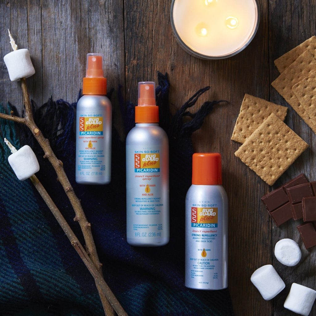Bottles of all three products in the Bug Guard Plus Picaridin insect repellant line artistically laid on a wooden surface, surrounded by the ingredients for smores and a large candle