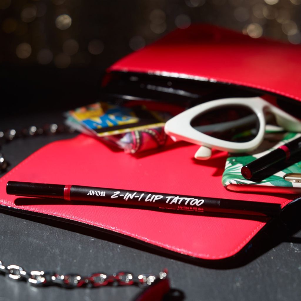 Open red purse with the contents spilling out including the Lip Tattoo Line & Fill Duo, sunglasses, a phone, and a wallet