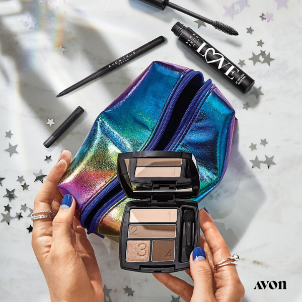 Woman's hands holding a compact of true color eyeshadow on top of a rainbow makeup bag, next to open eyeliner and mascara products artistically strewn on. marble countertop