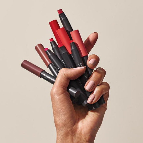 Woman's hand holding several tubes of Flat Velvet Lipstick, against a beige background