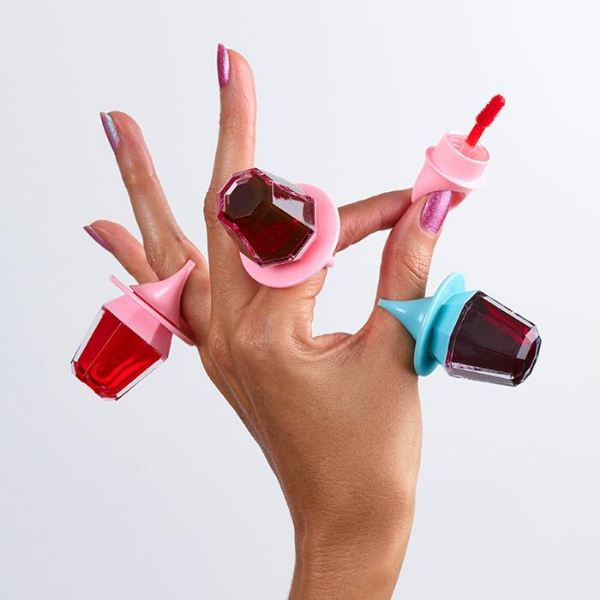 Woman's hand with the fingers stretched, wearing 3 containers of Put a Ring On It Lip Tint