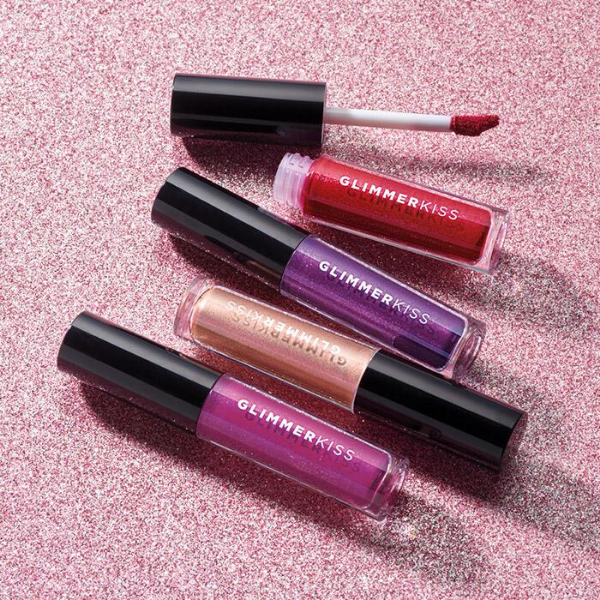 Four different tubes of Glimmerkiss Liquid Lipstick, against a sparkly pink background