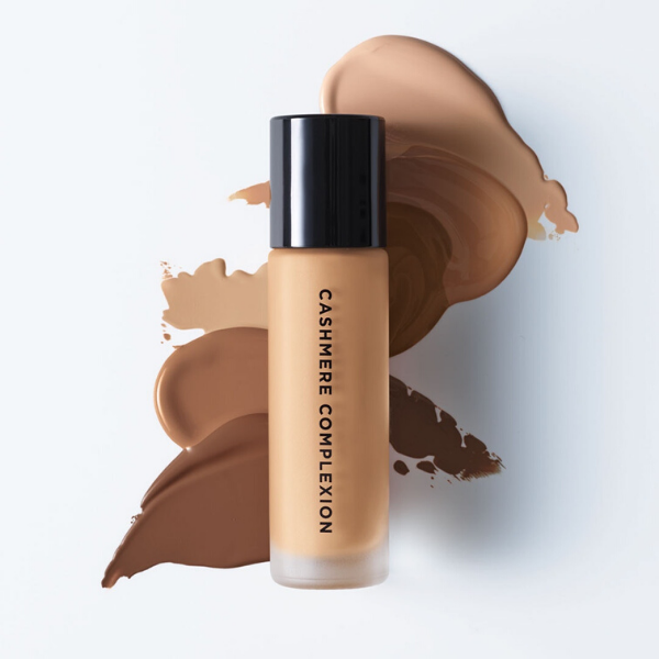 Tube of Cashmere Complexion Foundation on top of artistic foundation smears, against an off-white background