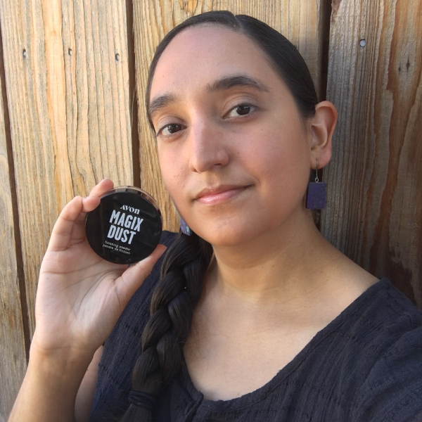 Woman looking at the camera as she holds up a container of Magix Dust finishing powder next to her face