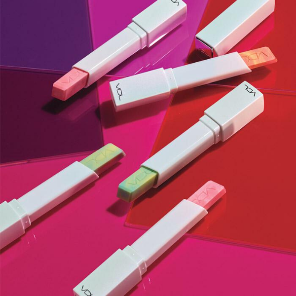 6 tubes of Lip Cube Marble Glow, artistically strewn on a bright pink surface with a loose pile of stage light gels