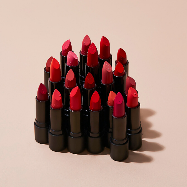 20 tubes of rouge satin lipstick arranged in a huddle with artistic drops of water, against a light beige background