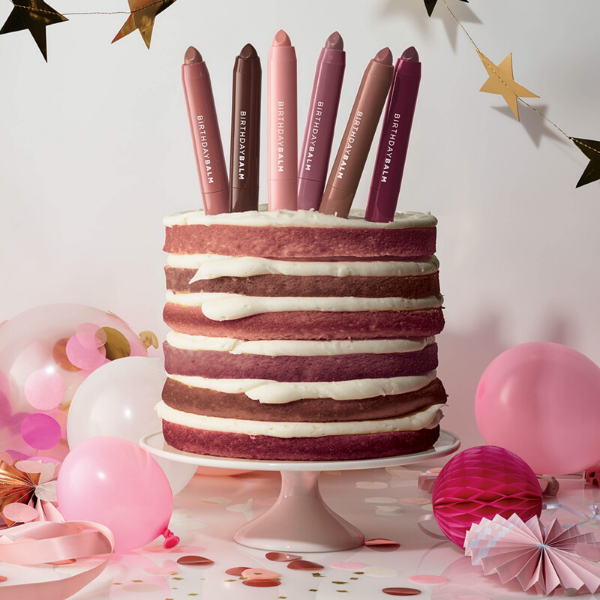 Layered cake with tubes of Birthday Balm artistically arranged on top like birthday candles