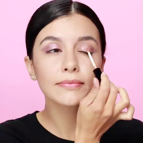 Woman in a black shirt applying a metallic liquid eyeshadow to her inner lid
