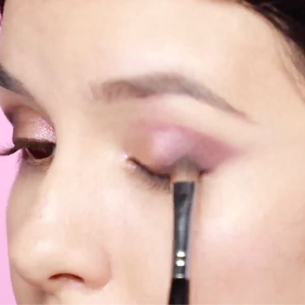 Close up of a woman's face as she applies eyeshadow to her outer lid