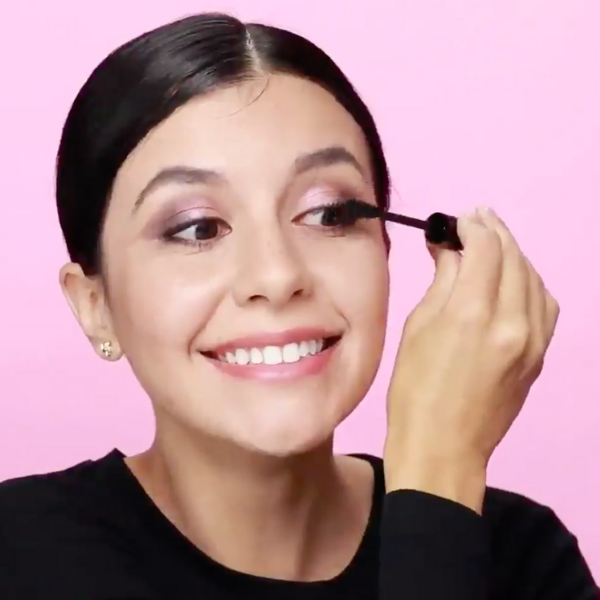 Woman in a black shirt applying mascara to her lashes