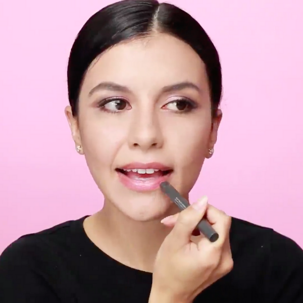 Woman in a black shirt applying light pink lipstick