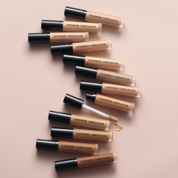 Row of avon liquid concealer tubes in various shades, agains a beige background