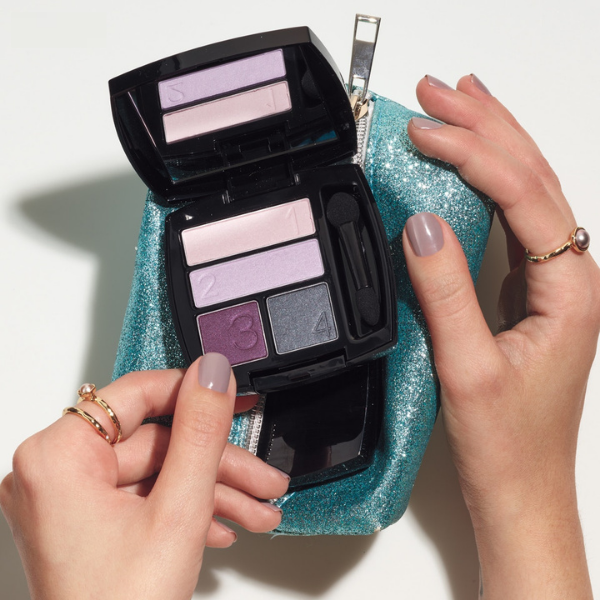 Compact of True Color Eyeshadow Quad, held up by a young woman's hands in front of a sparkly blue makeup bag