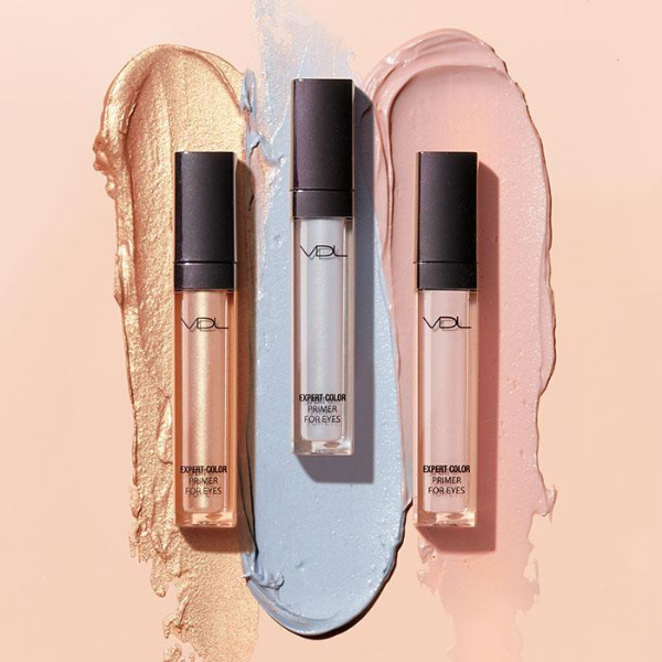 Three different tubes of VDL eye primer in front of artistic product smears, against a peach beige background