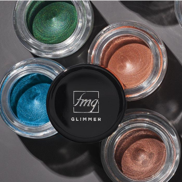 Four open pots of Glimmer Longwear Gel Eyeshadow, artistically strewn on a dark grey surface