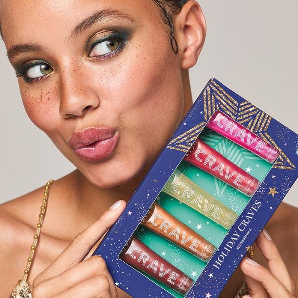 Model playfully pursing her lips and holding up a package of Holiday Craves Set, a lip gloss gift set