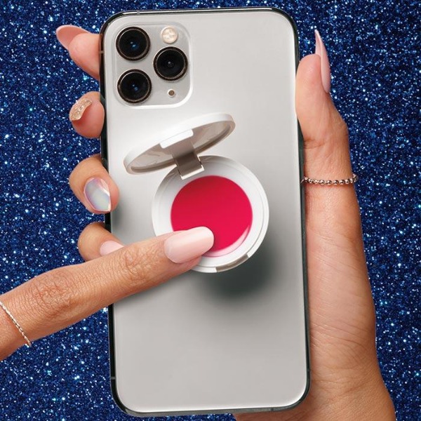 Back of a silver smartphone with a PopGrip lip balm in a bright pink shade, in front of a dark blue sparkle background