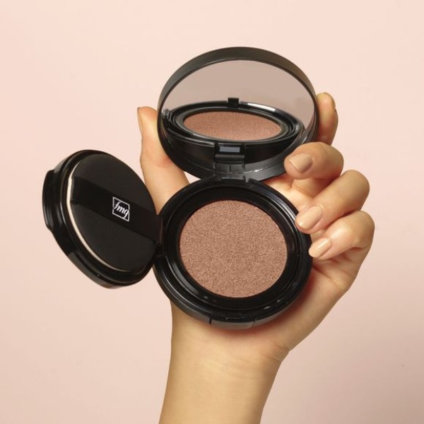Woman's hand with beige nailpolish holding an open compact of Cashmere Cushion Foundation, in front of a pale pink background