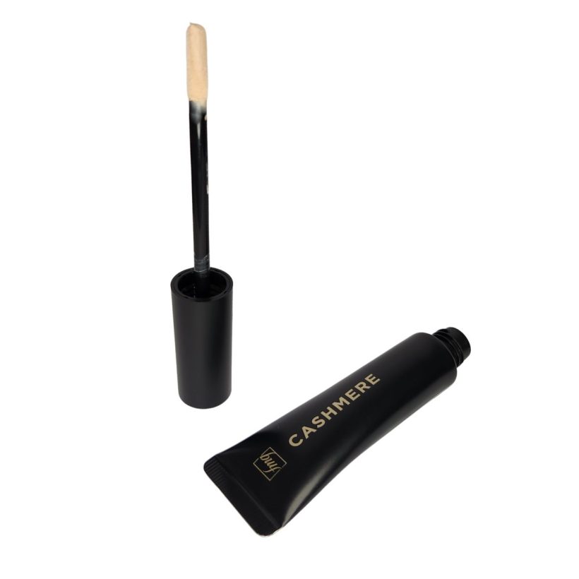 Open black tube with gold writing that says "fmg" and "Cashmere" sitting diagonally on its side, next to a cap with a doe foot style applicator that is covered with off-white cream liquid